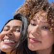 Two people pose cheek-to-cheek for a selfie in landscape mode, showcasing the wide field of view of Pixel 10's front camera