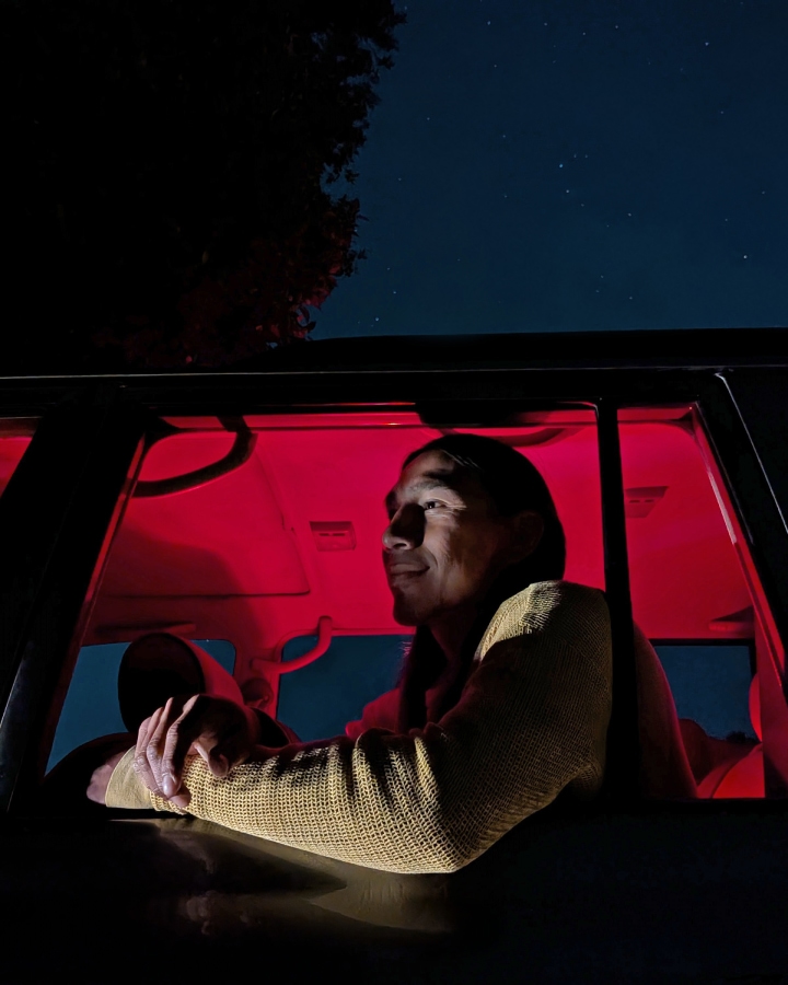 A person sits in a car during the night. The interior glows red.
